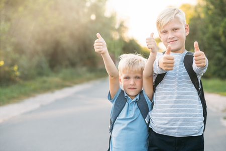 Two heerful blondy boys gives a thumbs-up. Schoolboys smiling and happy.の写真素材