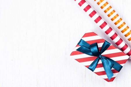 Christmas gift wrapped in striped gift paper tied with blue ribbon and two decorative paper rolls on white wooden background. New Year, holidays and celebration concept, top view with copy space.の写真素材