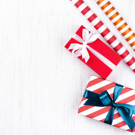 Christmas gift boxes wrapped in decorative striped and red paper tied with blue and white ribbons and two decorative paper rolls on white wooden background. Holidays concept, copy space.の写真素材