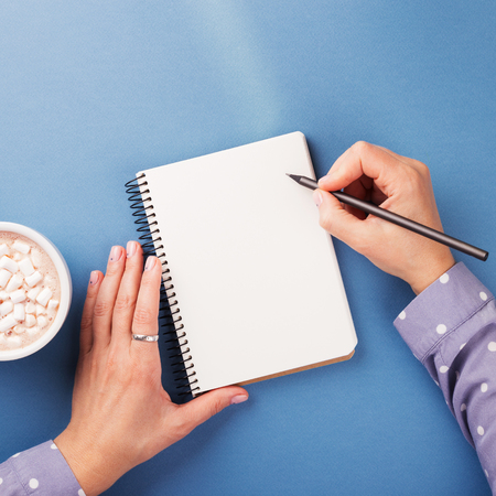 Womans hand writing in notebook on the blue background. Top view.の写真素材