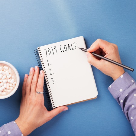 Womans hand writing 2019 Goals in notebook on the blue background. Top view.の写真素材