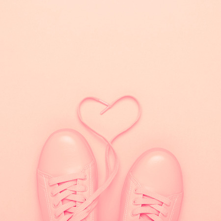 Pair of pink shoes with heart made of shoelaces on pink background. Trendy pastel color, monochrome image. Valentines card concept.の写真素材