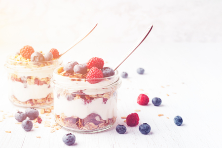Two jars with tasty parfait made of granola, berries and yogurt on white wooden table. Shot at angle. Toned image with copy space.の写真素材