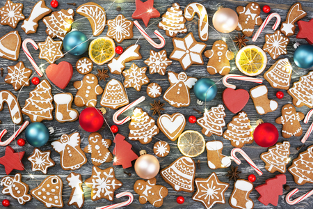 Christmas pattern made of gingerbread cookies, anise stars, allspices, berries, candy cane lollipops, Christmas balls, orange chips and wooden decorations with garland on wooden background. Flat lay.の写真素材