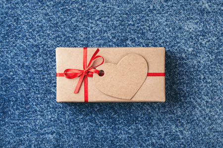 Kraft gift box with red bow and tag in shape of heart on blue jeans. Valentines day card.の写真素材