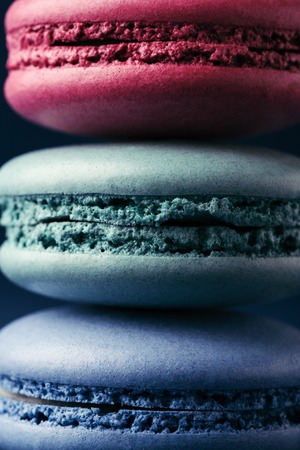 Stack of three colorful macarons on dark blue background. Close up view.の写真素材