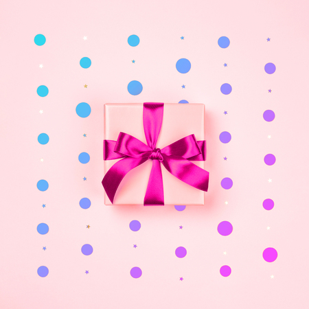 Pink gift box with neon pink bow on pink background with neon colored polka dots and sparkles. Holiday and Valentines minimal styled card concept.の写真素材