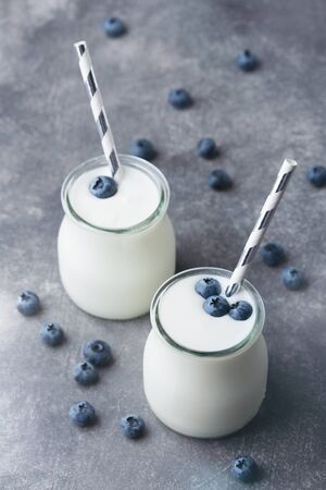 Greek yogurt with blueberries in a glass jar with paper straw on gray background. Healthy eating and dieting concept. Closeup view.の写真素材