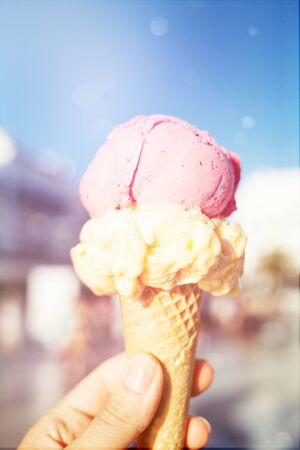 Womans hand holding ice cream in waffle cone. Strawberry and mango ice cream.の写真素材