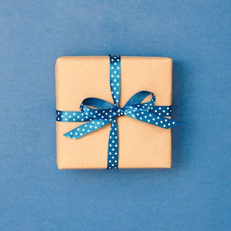 Gift box tied with classic blue ribbon in polka dots on blue background. Minimal styled greeting card in color of year.の写真素材