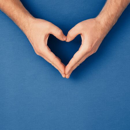 Male hands in shape of heart on classic blue background. Healthcare and chirty, color of year concept.の写真素材