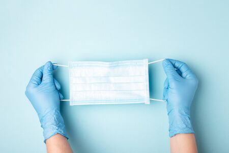 Hands in gloves showing medical face mask on blue background. Preventive measures to protect against...