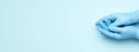 Doctors hands in medical gloves on blue background. Banner for website with copy space.の写真素材