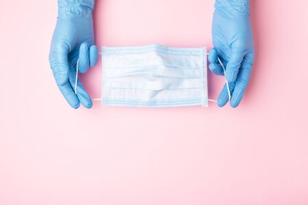 Hands in blue gloves showing medical face mask on pink background. Preventive measures to protect...