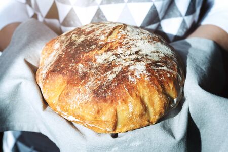 Hand holding fresh homemade bread on linen napkin. Traditional french bread.の写真素材