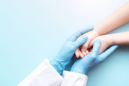 Doctor's hands in gloves holding child's hands. Medical care concept.の写真素材