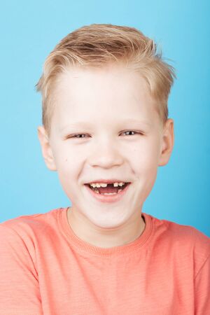 Cute laughing boy looking at the camera with stylish hairstyle in coral T-shirt, closeup, on blue background.の写真素材