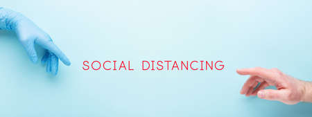 Social distancing concept with females hand in glove and mans hand on blue background. Two hands that want to touch each other.の写真素材