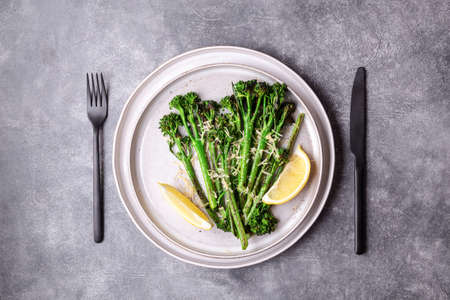 Roasted broccolini with lemon on the plate with black cutlery on stone table. Top view.の写真素材