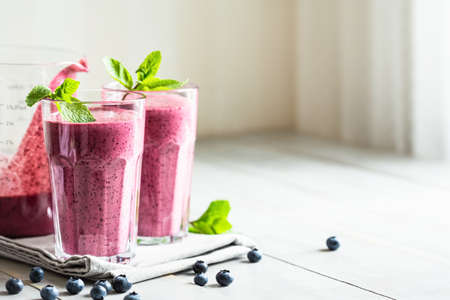 Two glasses of blueberry smoothie with mint garnish on the table.の写真素材