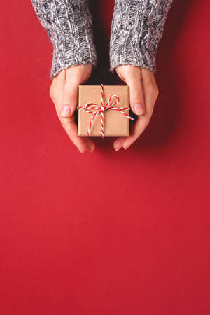 Females hands in pullover holding Christmas gift box on red background. Christmas and New Year greeting card.の写真素材