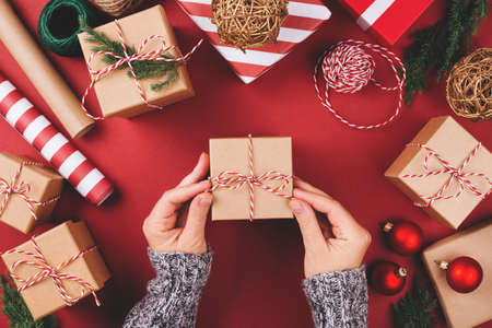 Christmas background with gift boxes and decorations on red. Preparation for holidays. Top view with copy space. Womans hands tying gift box.の写真素材