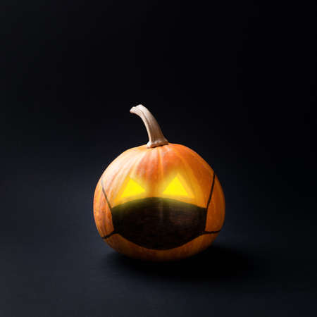 Halloween pumpkin in medical mask on black background. Lockdown concept.の写真素材