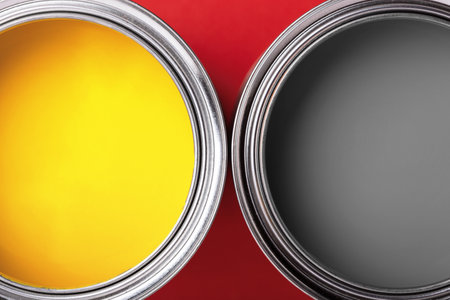 Cans of yellow and gray paint on red background. Top view, minimal.