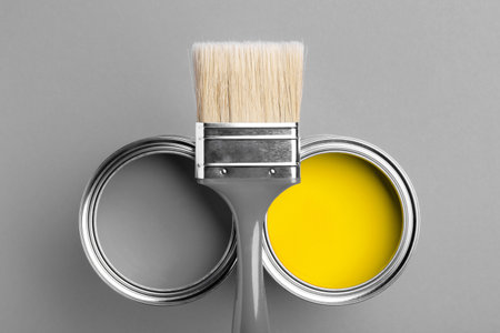 Two cans of yellow and gray paint with gray brush on gray background. Top view, repair concept.の写真素材
