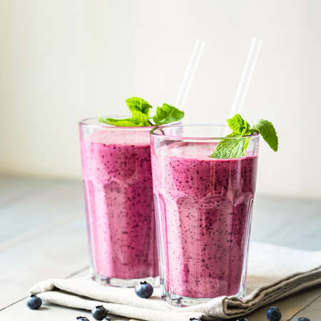 Two glasses of blueberry smoothie with mint garnish and straw on the table. Close up.の写真素材