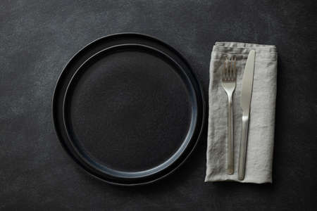 Empty black plates with silver cutlery and gray napkin on black table. Top view.の写真素材