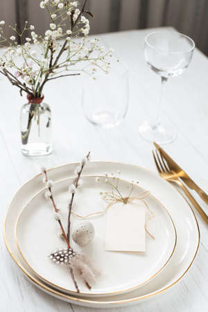 Easter table setting with willow twigs, quail eggs and tag. Golden cutlery and golden rim plates.の写真素材
