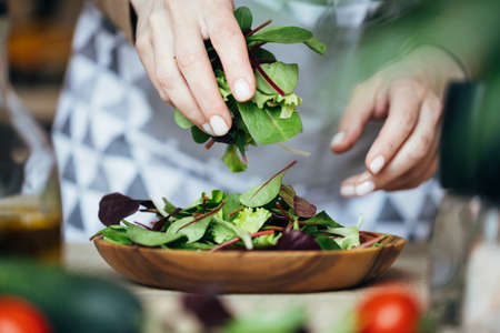 Woman putting a mix of salad on a wooden plate. Close up view.の写真素材