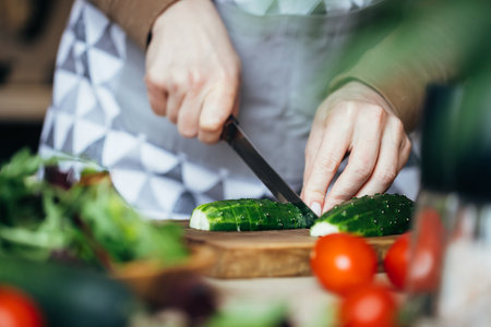 Woman cutting cucumber on wooden board. Close up view.の写真素材