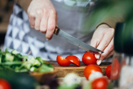 Woman cutting tometoes on wooden board. Close up view.の写真素材