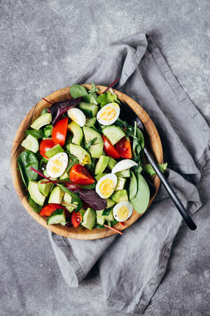 Healthy salad with tomatoes, avocado, cucumber and eggs on wooden plate.の写真素材
