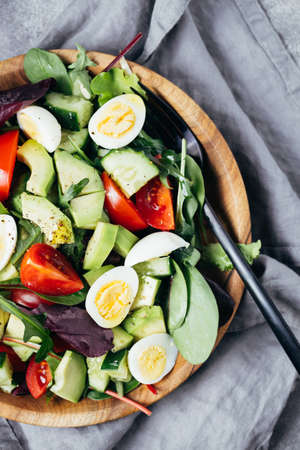 Close up view of salad with tomatoes, avocado, cucumber and eggs on wooden plate.の写真素材