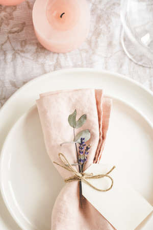 Close up view on plates arranged with a pink linen napkin, floral decor and tag on the table.の写真素材