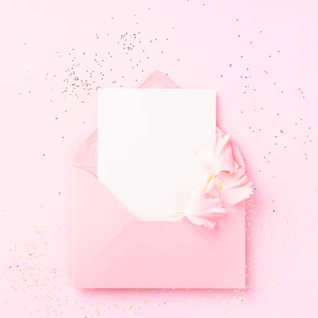 Blank white card in pink envelope with carnations petals on pink background with confetti.の写真素材