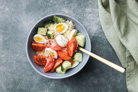 Vegan cous cous salad bowl with cucumber, cherry tomato and quail eggs on stone table.の写真素材