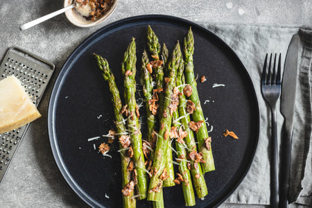 Roasted asparagus serving with almond nut petals and cheese on black plate.の写真素材