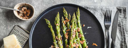 Roasted asparagus serving with almond nut petals and cheese on black plate.の写真素材