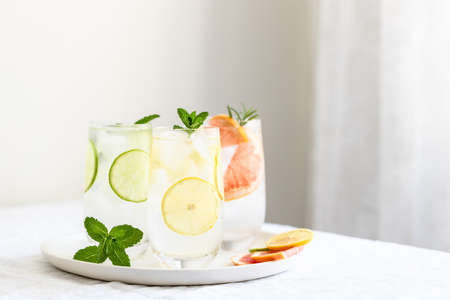 Glasses with cold citrus fruits water with mint garnish on plate.