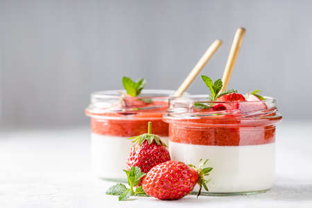 Panna cotta in glass jars with strawberry sauce and mint on white table.の写真素材