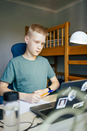 The young man is writing in a notebook while studying online.の写真素材