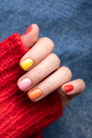 Female hand in red pullover with colorful manicure on jeans background.の写真素材