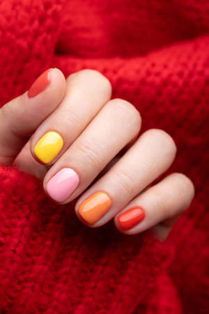 Female hand in red pullover with colorful manicure on red background.の写真素材