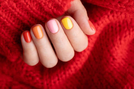 Female hand in red pullover with colorful manicure.の写真素材