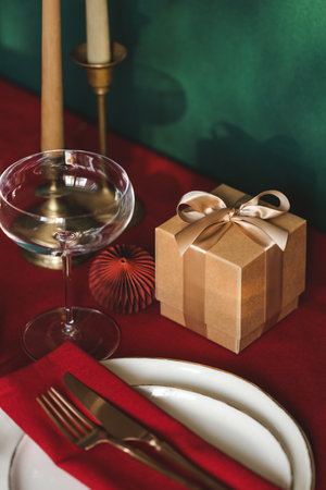 Christmas table setting among gift box and candles on red tablecloth. Concept of Christmas and New Year dinner.の写真素材