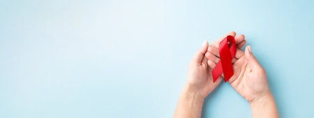 World AIDS Day banner with hands holding red ribbon on blue background.の写真素材